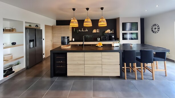 Een moderne keuken met een centraal eiland, inbouwapparatuur, hanglampen en een eethoek met barstoelen.
