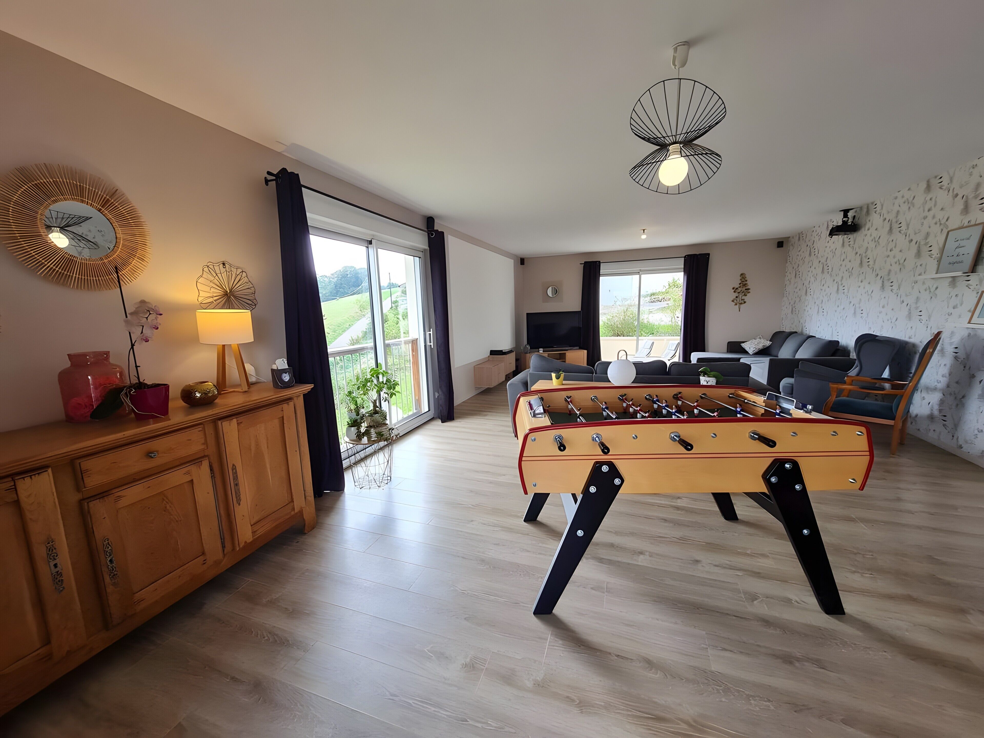 Un amplio salón con mesa de fútbol de mesa, televisor y sofá.