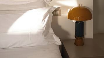 A neatly made bed with white linens and a modern lamp with a wooden base and a yellow lampshade on a bedside table.