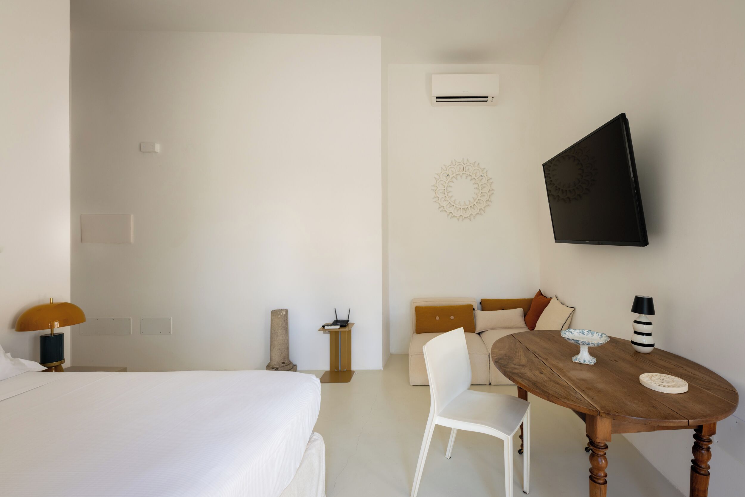 A hotel room with a bed, a small table with a lamp, a sofa, and a wall-mounted TV.