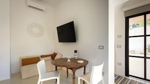 Una sala de estar moderna con una mesa redonda de madera, sillas blancas, un sofá beige con cojines marrones, un televisor de pantalla plana montado en la pared y un adorno mural.