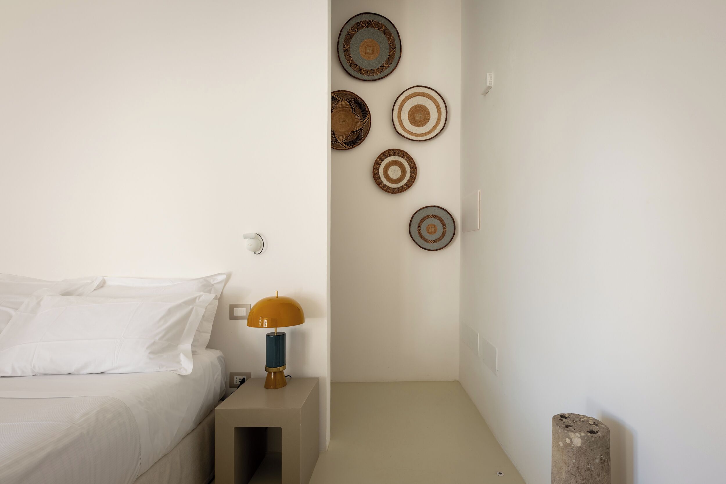Un dormitorio con cama, mesita de noche con lámpara y placas decorativas en la pared.