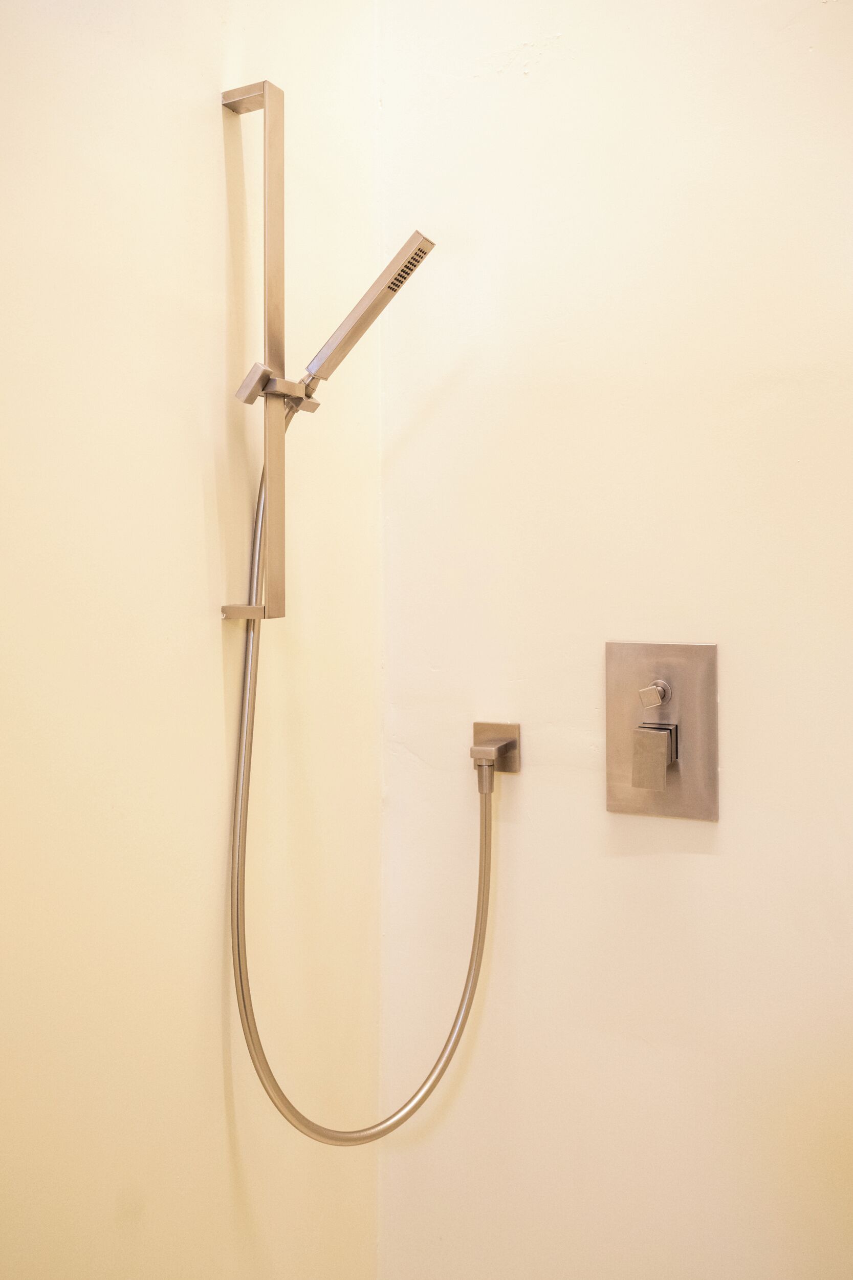A modern shower with a handheld showerhead and a fixed showerhead, mounted on a wall with a control panel.