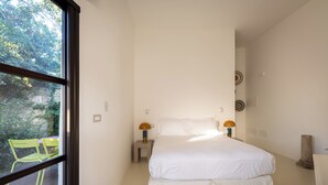 Un dormitorio con un ventanal grande, una cama, dos mesitas de noche con lámparas y una silla al lado.