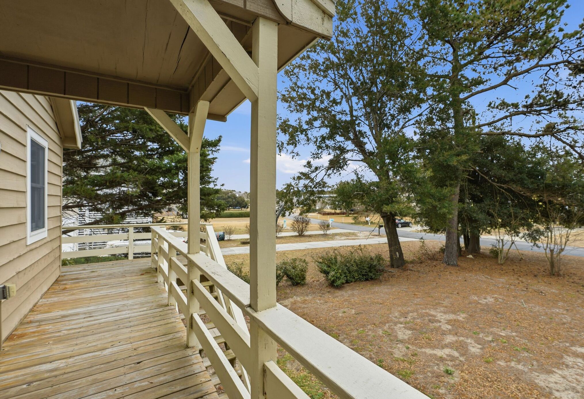 A wooden deck with a railing, leading to a house with a covered porch.