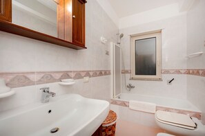 Ein Badezimmer mit einem großen Waschbecken, einem Spiegel, einer Dusche und einer Toilette.