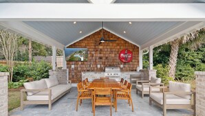 Een terras buiten met een houten tafel en stoelen, een barbecue en een Coca-Cola bord.