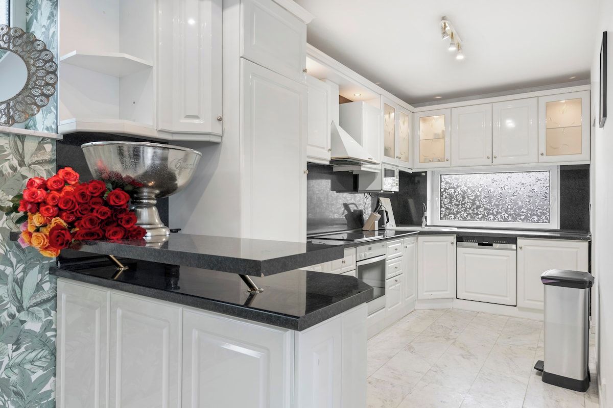 A modern kitchen with white cabinetry, a black countertop, and a stainless steel sink.
