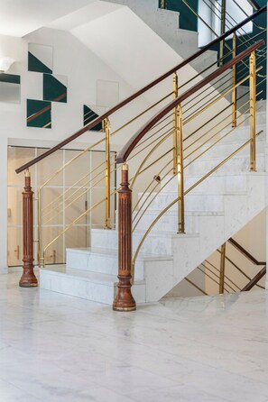 A grand staircase with marble steps and wooden balusters, leading to a second-floor landing.