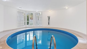 Ein Hallenbad mit großen Glaswänden, gefliestem Boden und einer Decke mit eingelassener Beleuchtung.