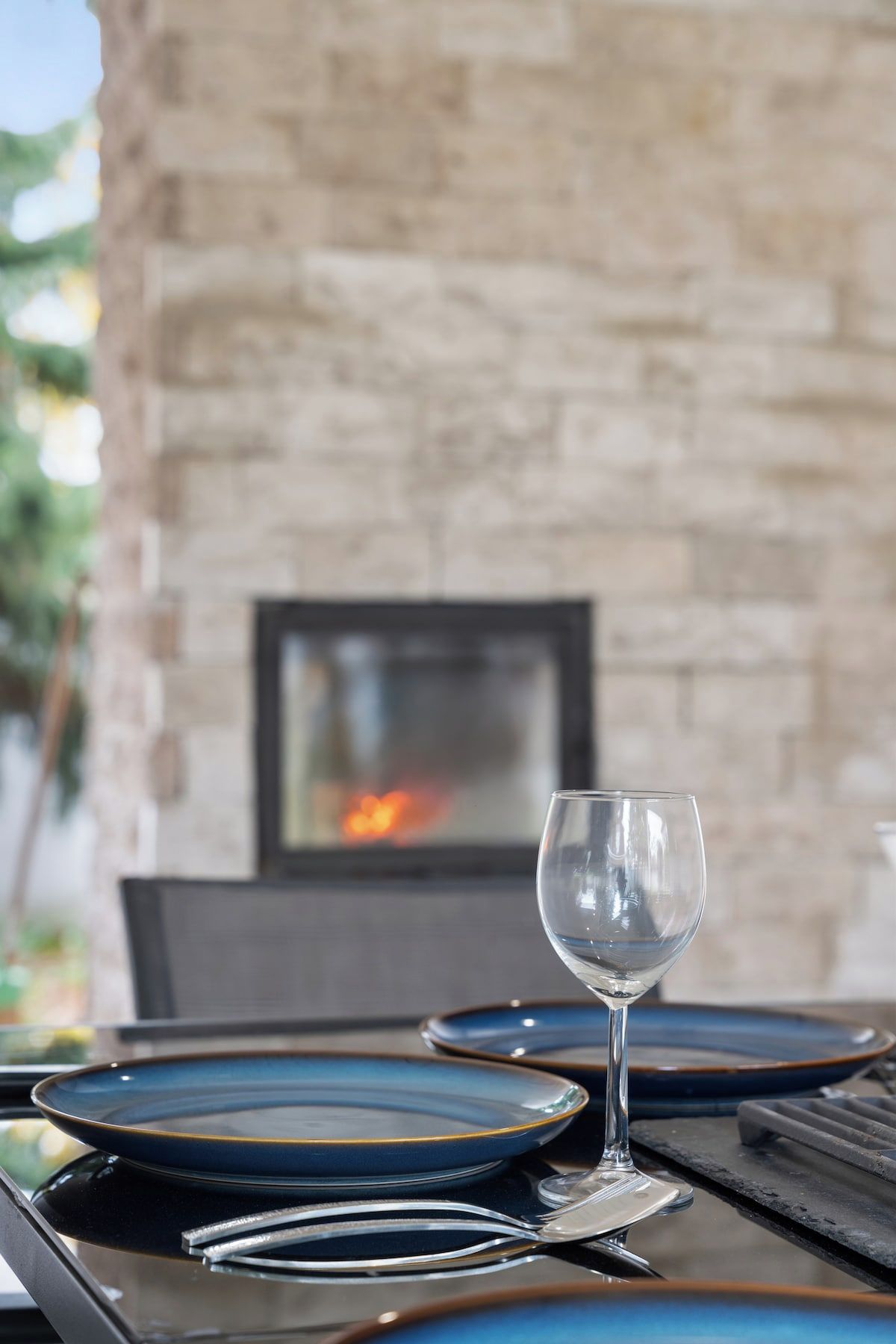 A table set with blue plates and a wine glass, with a stone wall and a fireplace in the background.