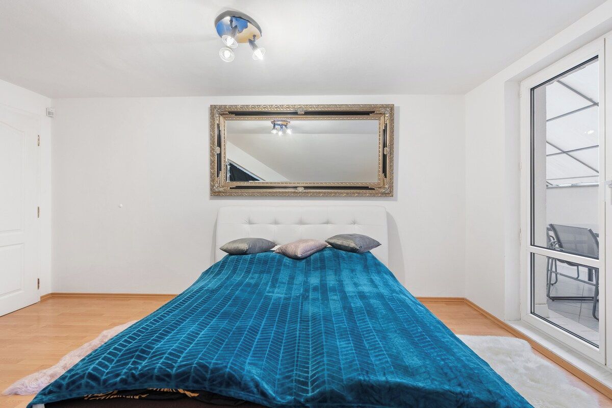 Et soveværelse med seng, et stort spejl, et vindue og en loftlampe.