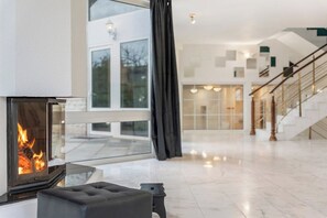 A modern interior with a fireplace, a staircase, and a view through large windows. - Black Dragon Castle (Prague 20)