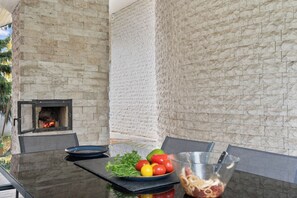 An outdoor dining area with a stone wall, a fire feature, and a table with food and utensils.