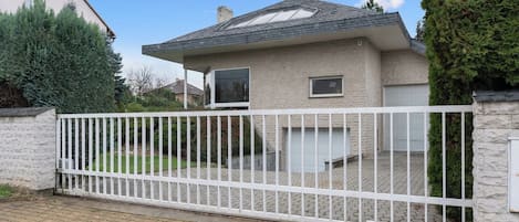 A residential property with a gated entrance, a paved driveway, and a house with a sloped roof.
