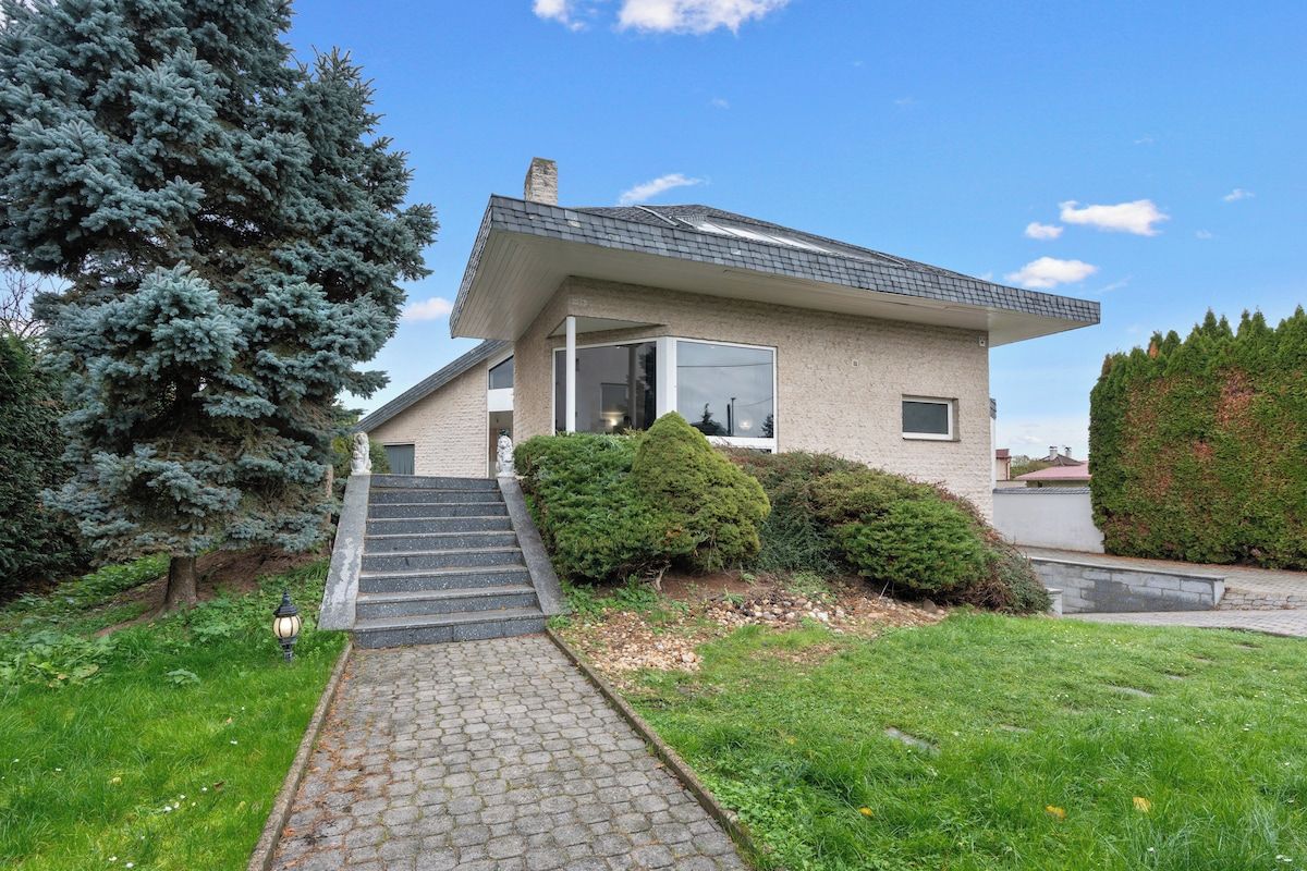 A modern house with a sloped roof, a front entrance, and a paved driveway leading to the door.