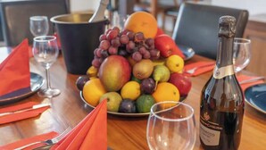 Una mesa de comedor servida con platos, servilletas, un frutero, copas de vino y una botella de vino.