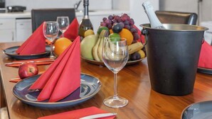 Una mesa de comedor con platos, vasos, un frutero y una botella.