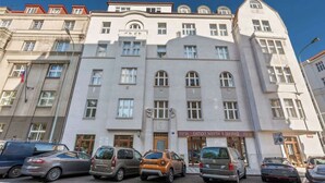 Un edificio de varios pisos con una entrada central y varios coches aparcados en la parte delantera.