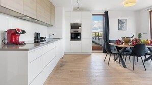 Ett modernt kök med vita skåp, en röd kaffebryggare och en matplats med ett bord som är dukat för fyra personer.