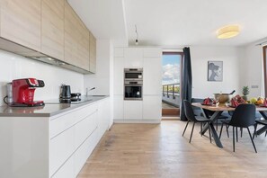 A modern kitchen with white cabinets, a red coffee maker, and a dining area with a table set for four. - Terrace ONE (Prague 7)