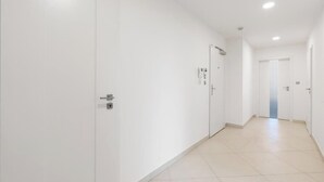 En lång, smal hall med vita väggar och dörrar, som leder till ett rum med en dörr längst in.
