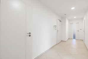 A long, narrow hallway with white walls and doors, leading to a room with a door at the end. - Terrace ONE (Prague 7)