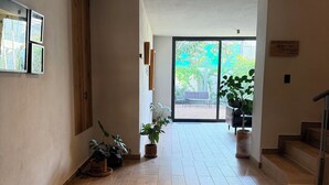 Un ampio corridoio con pavimento in legno, piante in vaso e un'ampia porta scorrevole in vetro che dà su uno spazio all'aperto.