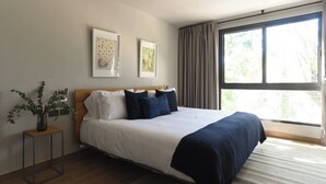 Una camera da letto con un letto, un comodino, un vaso con piante e due quadri appesi al muro.