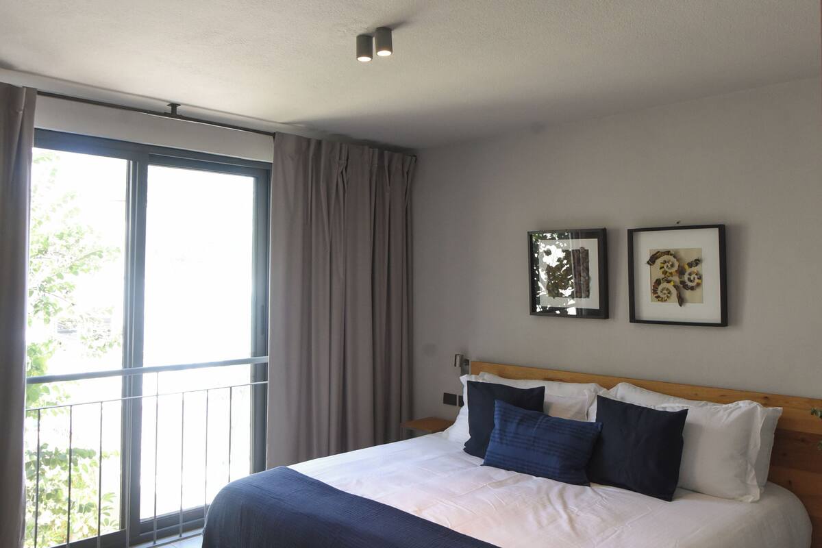 Una habitación de hotel con una cama grande, un balcón y dos cuadros en la pared.