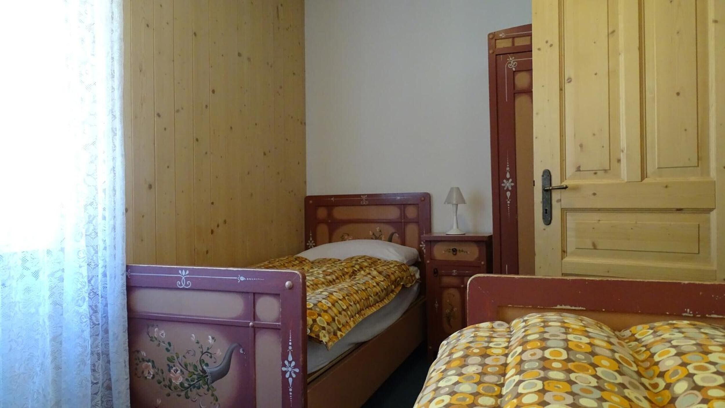 Ein Zimmer mit zwei Betten, einem Holzschrank und einem kleinen Nachttisch mit Lampe.