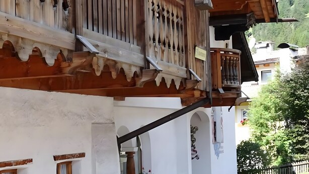 Un edificio in legno tradizionale con un balcone, un cortile lastricato in pietra e uno sfondo montuoso.