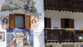 Un edificio con un balcone in legno, una finestra con tenda e un murale con figure religiose.