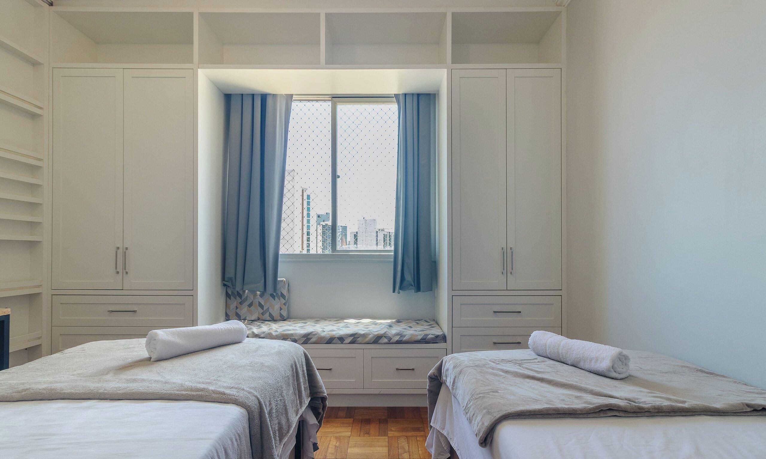 A bedroom with two beds, a window with curtains, and a city view.