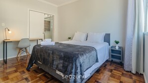 Ein Schlafzimmer mit Bett, Schreibtisch, Stuhl, Spiegel und einer kleinen Pflanze.