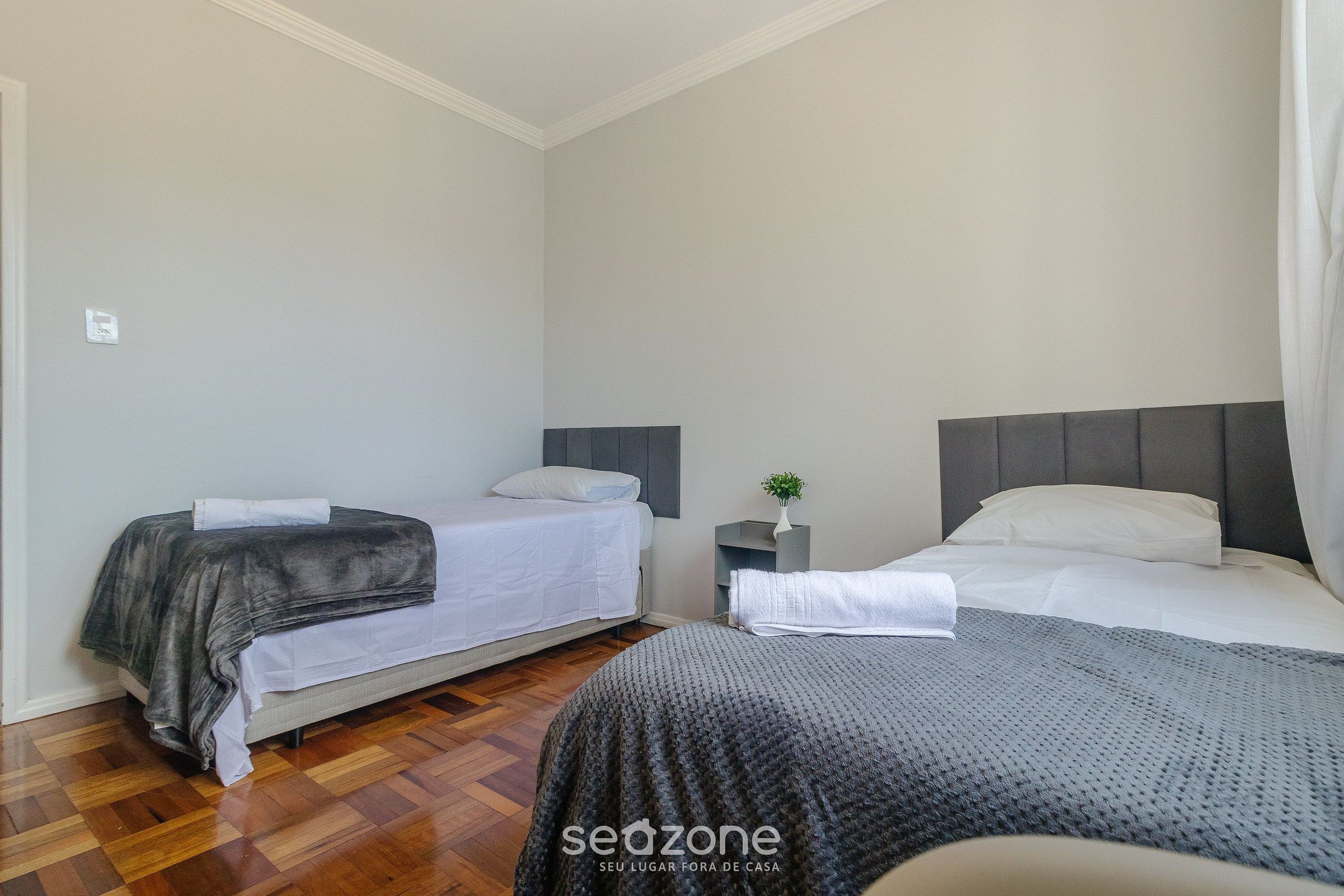 A bedroom with two beds, a nightstand, and a small plant.