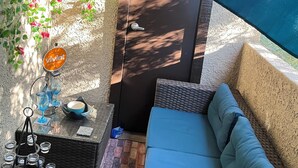 Ein gemütlicher Sitzbereich im Freien mit einer gepolsterten Bank, einem kleinen Tisch mit Schüssel und Gläsern sowie einer mit Kletterpflanzen bewachsenen Wand.