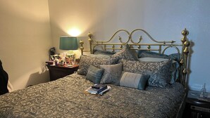 Ein ordentlich bezogenes Bett mit einem gemusterten Überwurf, ein Nachttisch mit Lampe und eine Wandleuchte.