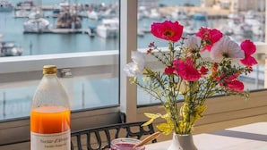 Una mesa con un frasco de jugo de naranja, un tarro de mermelada, un florero de flores y un plato de fruta.