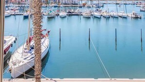 Un puerto deportivo con numerosas embarcaciones amarradas, cielo despejado y una palmera en primer plano.