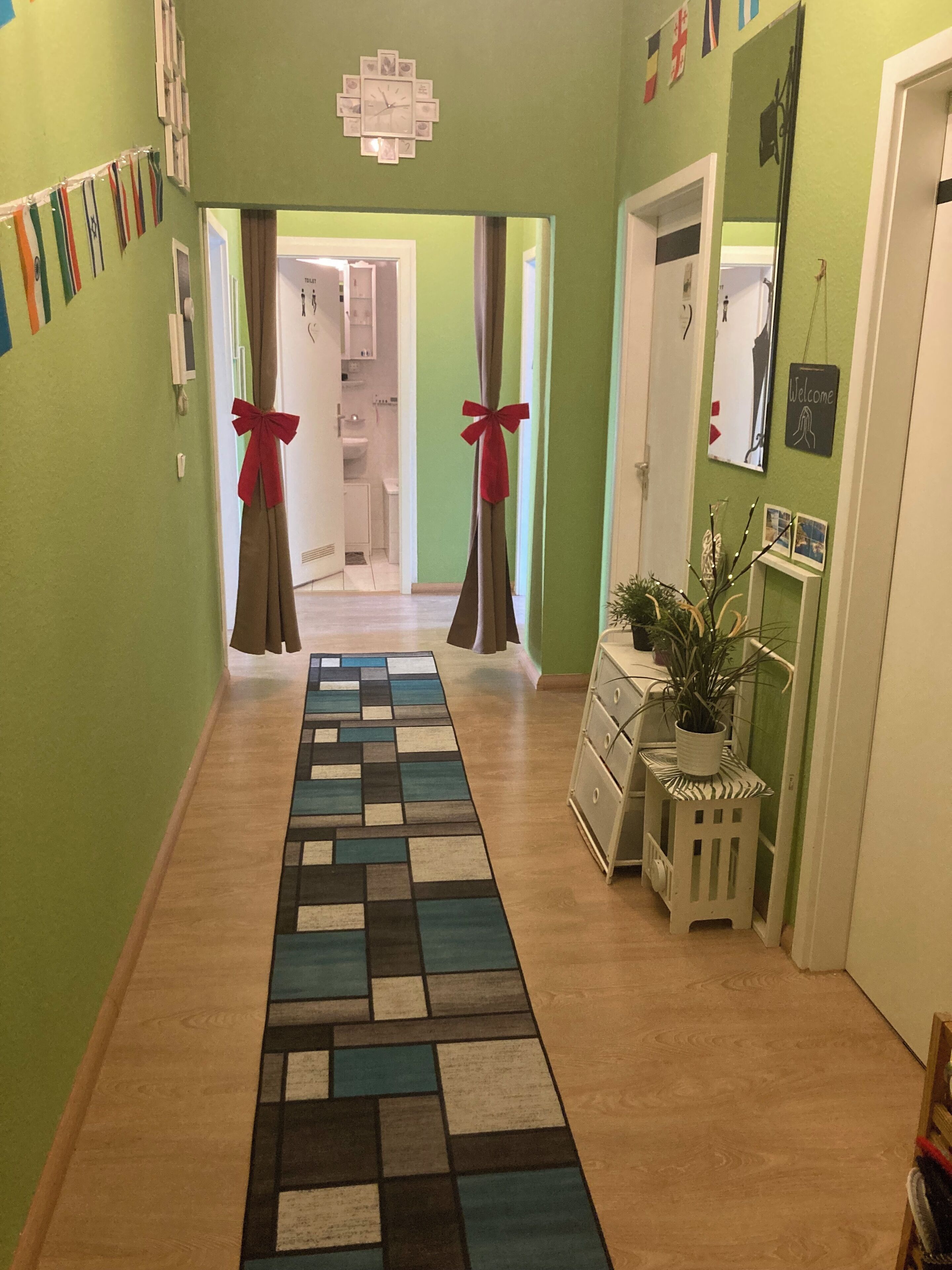 A hallway with a patterned rug, a plant on a side table, and a welcome sign on the wall.