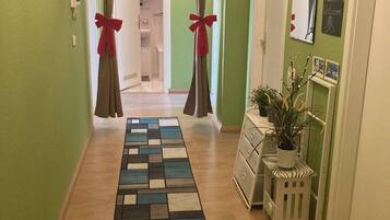 A hallway with a patterned rug, a plant on a side table, and a welcome sign on the wall.
