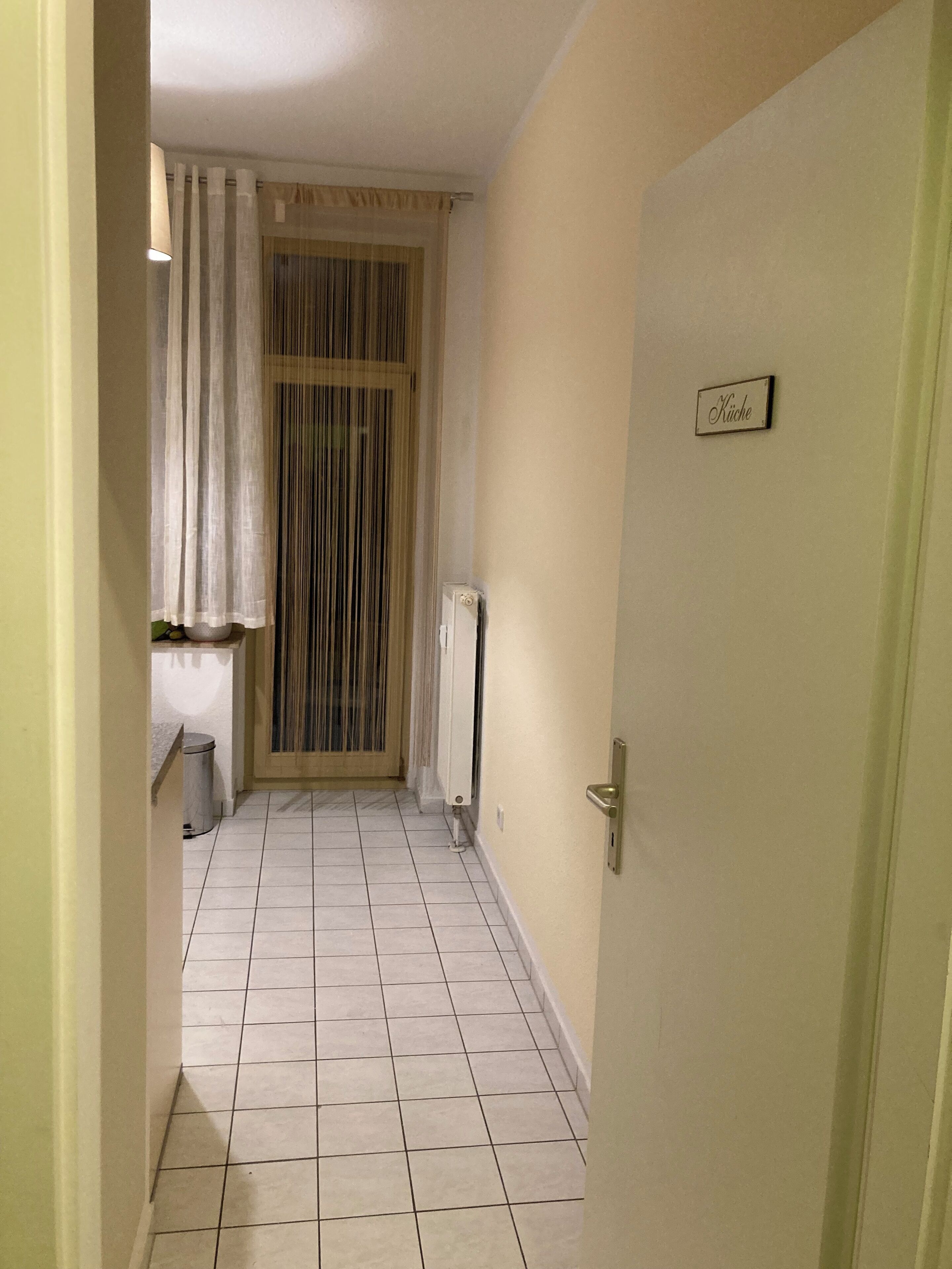 A narrow hallway with a tiled floor, a radiator, and a door with a sign that reads "Küche".