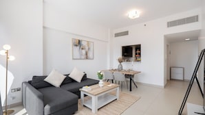 En moderne stue med en grå sofa, et sofabord og et spiseområde med et bord dækket til fire personer.