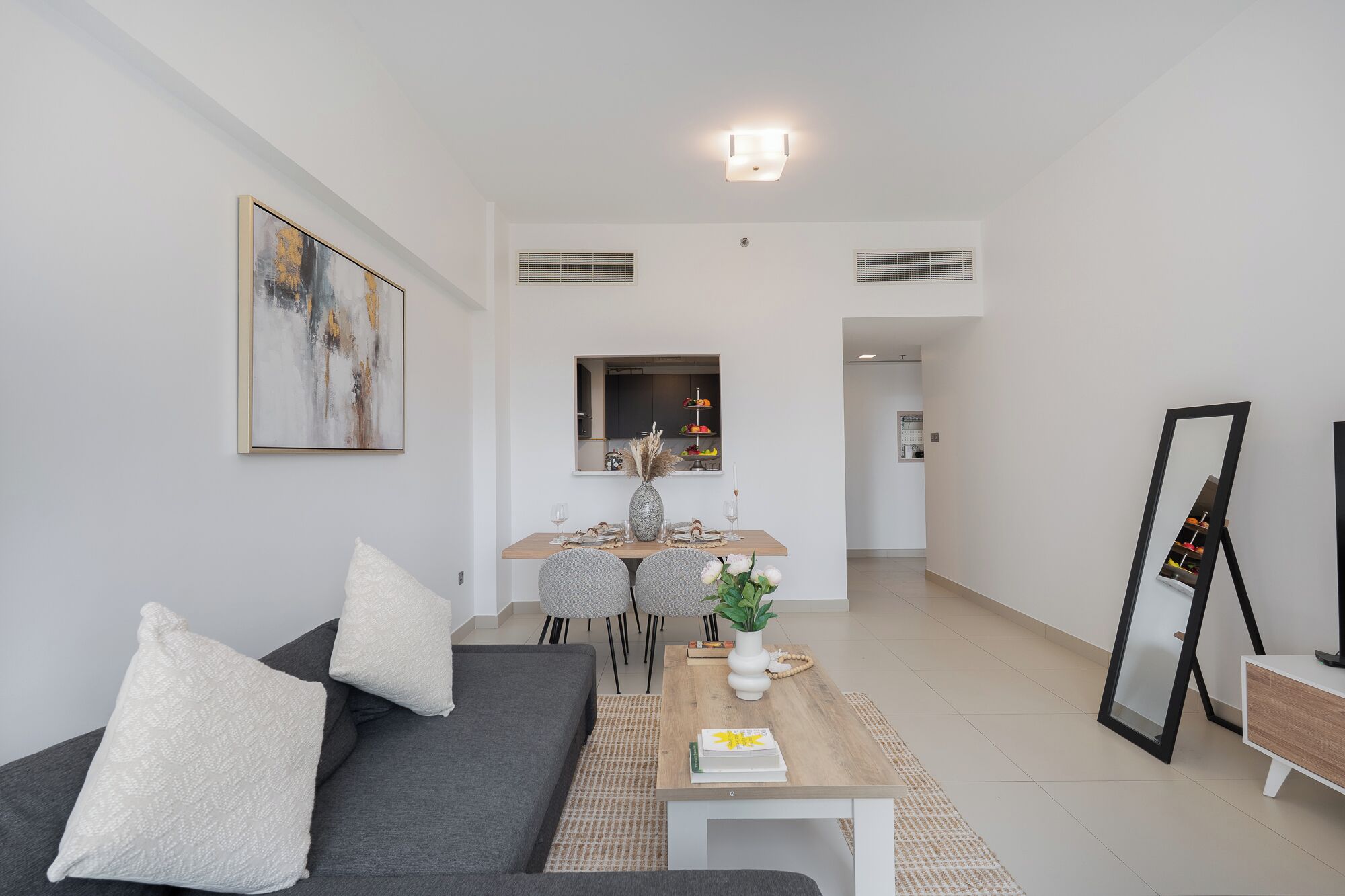 Un salon moderne avec un canapé gris, une table basse et un coin repas comprenant une table et des chaises en bois.