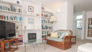 Una sala de estar con televisión, estanterías, un sofá de mimbre, una mesa de centro de vidrio y una chimenea.