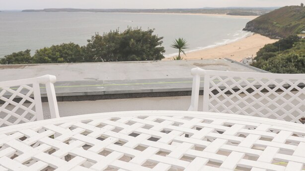 Vista al mar desde un balcón con una mesa de entramado blanco.
