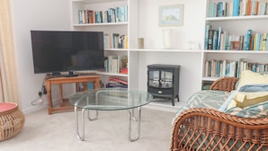Una sala de estar con una mesa de vidrio, muebles de mimbre, un televisor y estanterías llenas de libros.