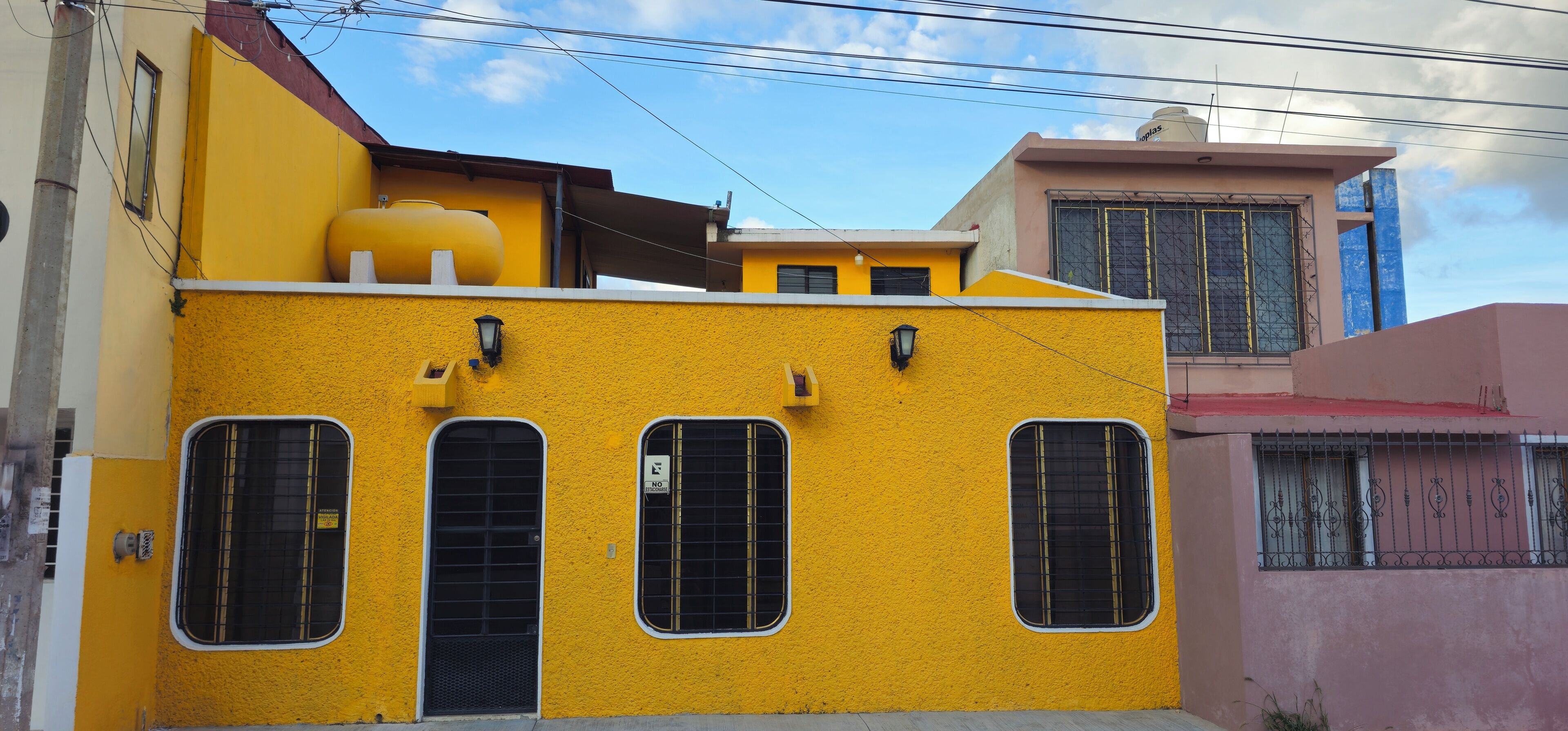 A yellow building with three windows and a water tank on the roof.