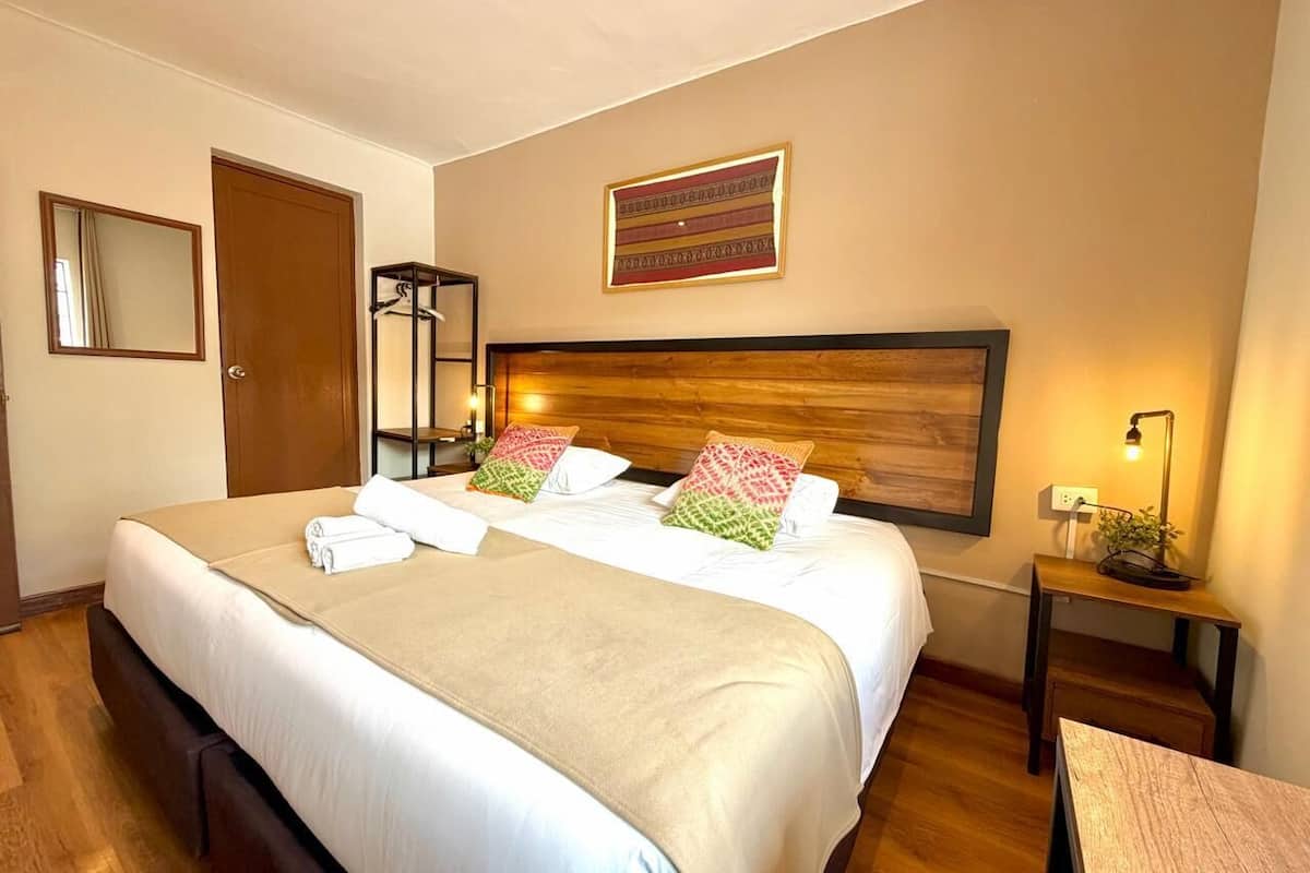Ein Hotelzimmer mit einem großen Bett, einem hölzernen Kopfteil, einem Nachttisch mit Lampe und einem Spiegel an der Wand.